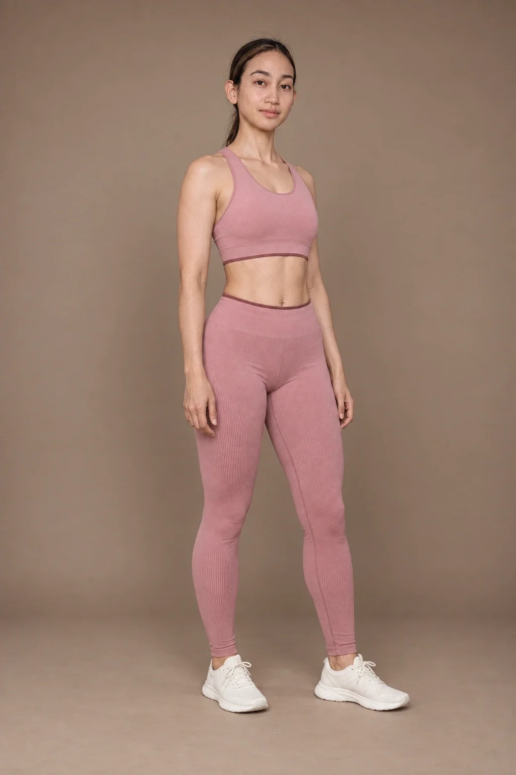 Full-length studio portrait of a model in a rose workout set and off-white trainers